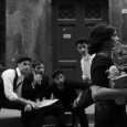 Four young men loiter outside the door of a building in a Neapolitan street. They’re passing time between animated chatting, drags of their cigarettes and joking around. The place they […]